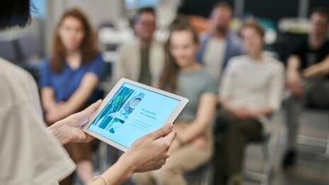 Frau liest auf Tablet, Seminarteilnehmende schauen zu